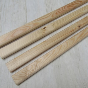 May include: Four unfinished wooden dowels, each with a natural wood grain pattern. The dowels are light in color and appear to be made of pine or a similar softwood. The ends are cut cleanly, and the dowels are arranged diagonally.