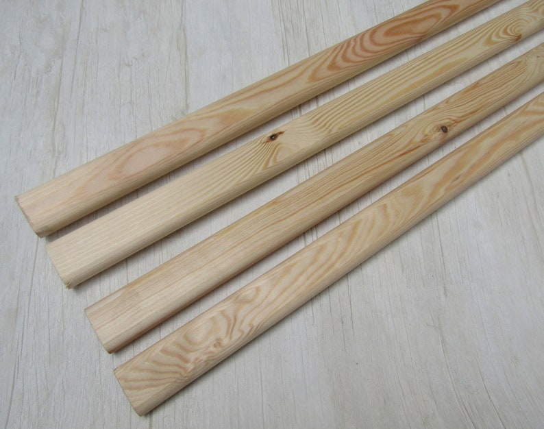 May include: Four unfinished wooden dowels, each with a natural wood grain pattern. The dowels are light in color and appear to be made of pine or a similar softwood. The ends are cut cleanly, and the dowels are arranged diagonally.