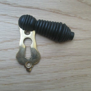May include: A black wooden door knob with a brass keyhole escutcheon. The knob has a ribbed design.