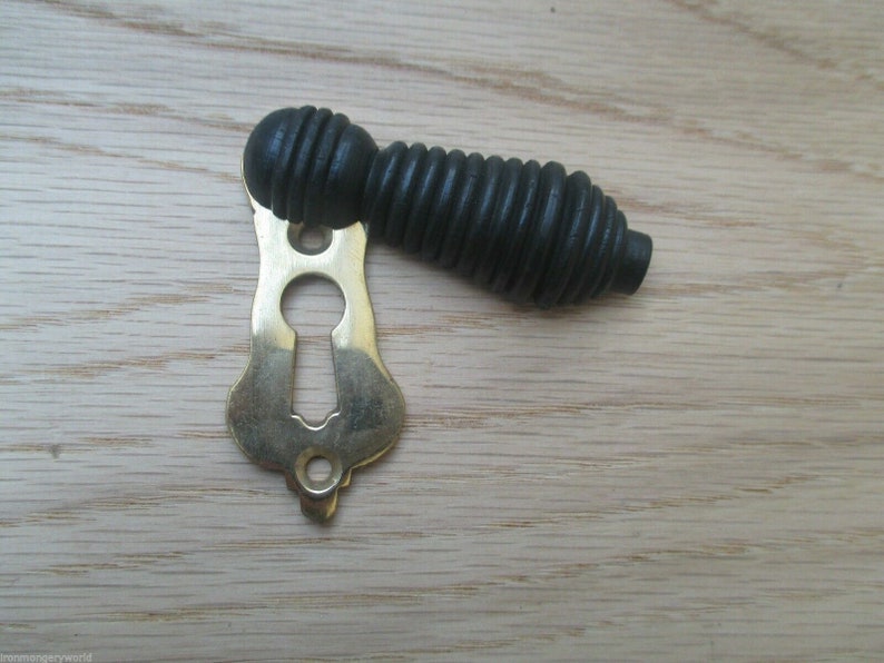 May include: A black wooden door knob with a brass keyhole escutcheon. The knob has a ribbed design.