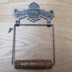 May include: Cast iron toilet paper holder with a wooden roller and a decorative metal sign that reads "TRADE MARK ST PANCRAS FIXTURE WBF & SO LONDON N".