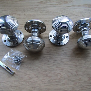 May include: Four polished chrome door knobs with a ribbed design. The knobs are on a wooden surface with a small bag of screws.
