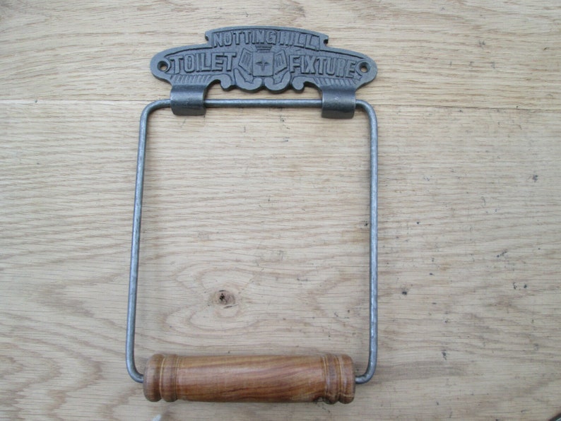 May include: A cast iron toilet paper holder with a wooden roller. The holder has a sign that reads "NOTTING HILL TOILET FIXTURES".