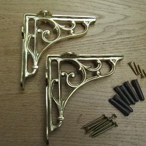 May include: Two gold metal shelf brackets with a decorative scroll design. The brackets come with screws and wall anchors.