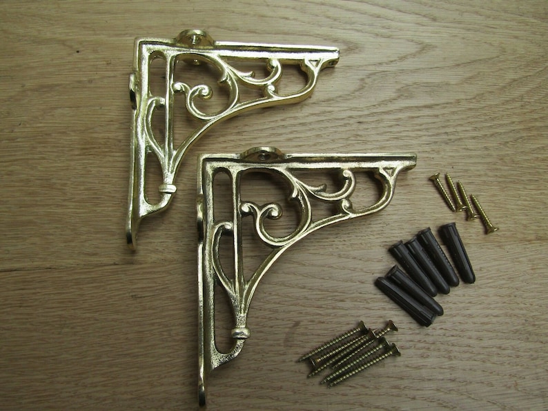 May include: Two gold metal shelf brackets with a decorative scroll design. The brackets come with screws and wall anchors.