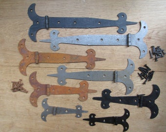 May include: Assortment of eight antique-style hinges in various finishes, including black, silver, and rust. The hinges are made of metal and have a decorative, ornate design. Some of the hinges are accompanied by small piles of screws.