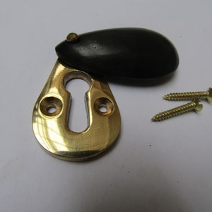 May include: A brass keyhole cover with a black wooden escutcheon. The cover is designed to be used with a door lock and comes with two screws.