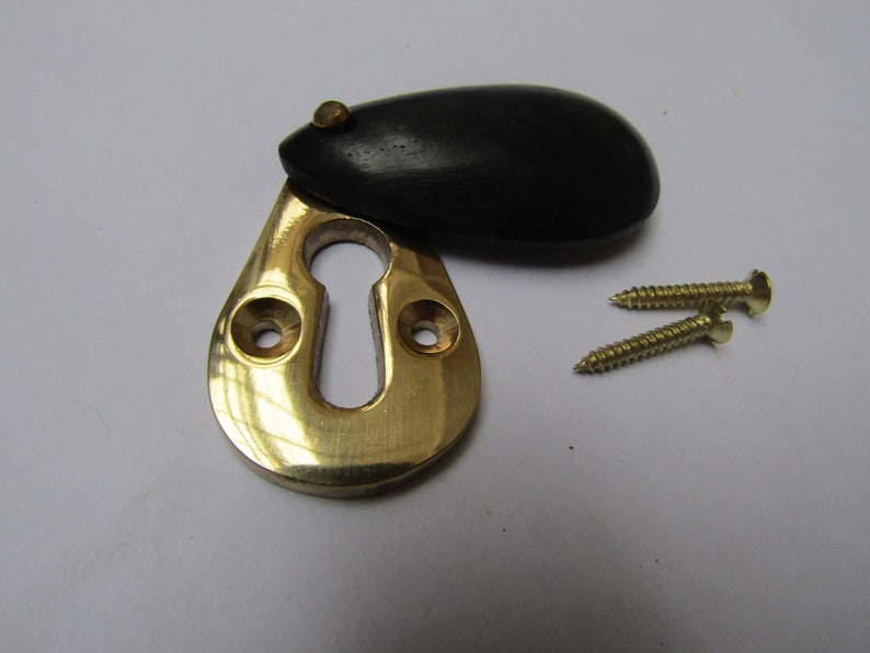 May include: A brass keyhole cover with a black wooden escutcheon. The cover is designed to be used with a door lock and comes with two screws.