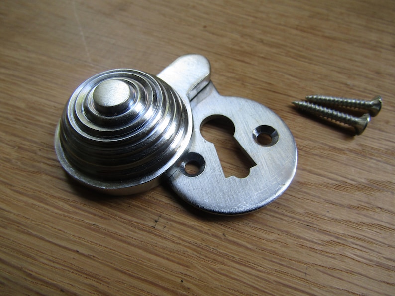 May include: Silver keyhole cover with a decorative, ridged, round escutcheon. The cover is designed to be mounted on a door or cabinet. Two screws are included.