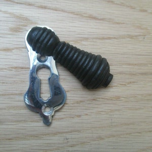 May include: A black, ribbed, decorative door knob with a silver keyhole cover. The knob is on a wooden surface.