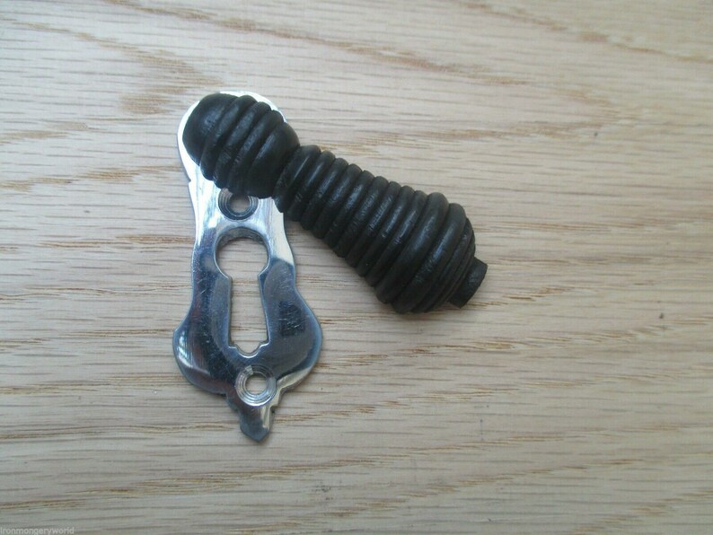 May include: A black, ribbed, decorative door knob with a silver keyhole cover. The knob is on a wooden surface.