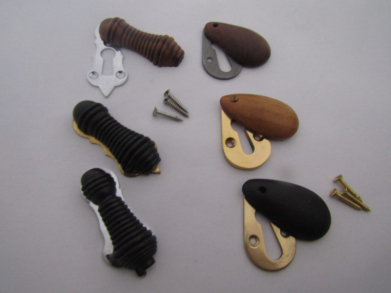 May include: Assortment of keyhole covers in various finishes, including wood, black, and brass. Some covers are oval shaped with a keyhole cut out, while others are cylindrical with a ribbed texture. The covers are accompanied by small screws for installation.