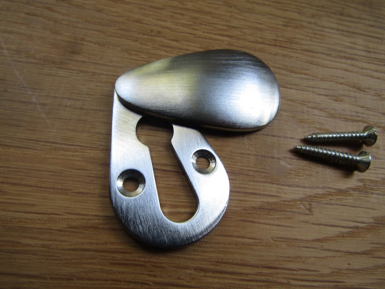 May include: A silver keyhole cover with a rounded, teardrop-shaped flap. The cover is designed to conceal a keyhole and is secured with two screws.