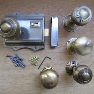 Może przedstawiać: Zestaw antycznych mosiężnych gałek drzwiowych i zasuwki z wkrętami i kluczem imbusowym. Gałki mają okrągły kształt z żebrowanym wzorem.