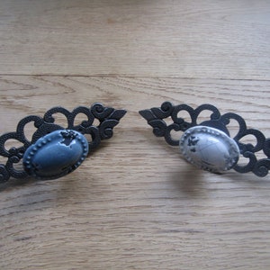 Könnte beinhalten: Zwei verzierte schwarze Metall-Schubladengriffe mit ovalen Keramikknöpfen. Ein Knopf ist blau und der andere ist weiß.