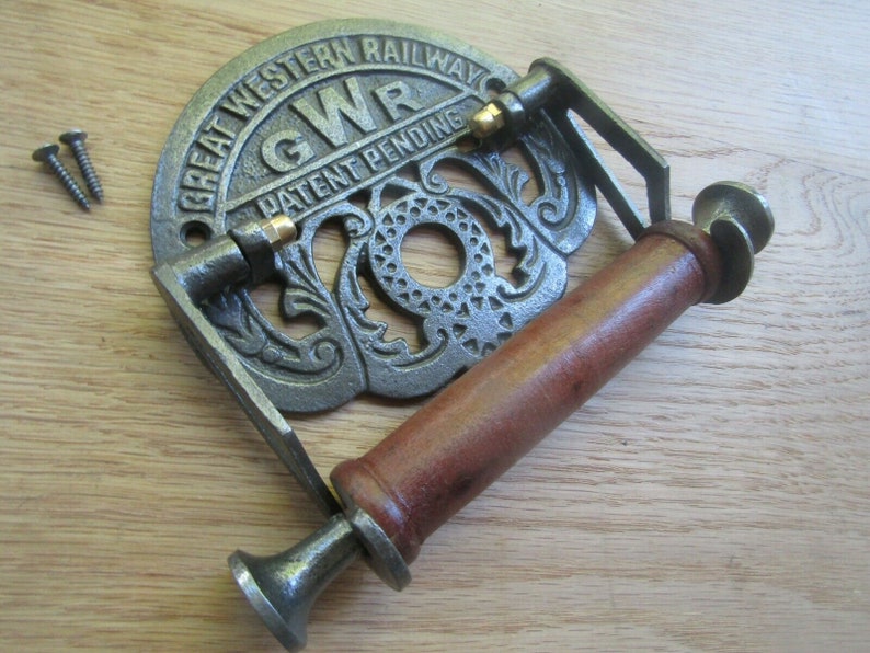 May include: Cast iron toilet paper holder with a wooden roller and a Great Western Railway logo. The holder is painted in a silver color and has a decorative design. The logo reads "Great Western Railway" and "GWR Patent Pending".