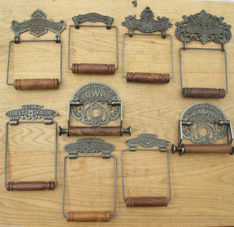 May include: Nine antique cast iron toilet paper holders with wooden dowels. The holders feature ornate designs and various company names, including "St Pancras Fixture", "Great Western Railway GWR", "Victoria Toilet Fixture", and "Waterer Toilet Fixture".