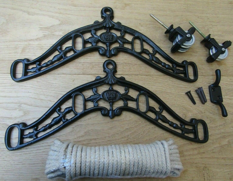 May include: A black cast iron clothesline pulley system kit. The kit includes two decorative brackets, pulleys, screws, wall anchors, and a coil of rope. The brackets have an ornate design with floral and crown details.