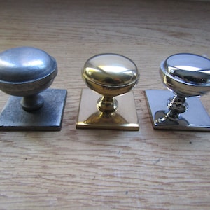 Pode incluir: Três botões de armário com bases quadradas. Os botões são feitos de metal e são acabados em prata, ouro e cromo.