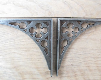 Puede incluir: Dos soportes de estante de metal plateado con un diseño decorativo e intrincado. Los soportes tienen forma de ángulo recto y presentan un patrón floral.