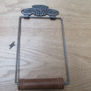 May include: A vintage cast iron toilet paper holder with a wooden roller. The holder has a decorative top with the text "VICTORIA TOILET FIXTURE CO."