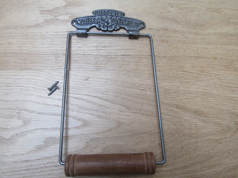 May include: A vintage cast iron toilet paper holder with a wooden roller. The holder has a decorative top with the text "VICTORIA TOILET FIXTURE CO."