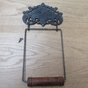 May include: Black cast iron toilet paper holder with a decorative scroll design and the word "Toilet" on the top. The holder has a wooden dowel for hanging the paper roll.