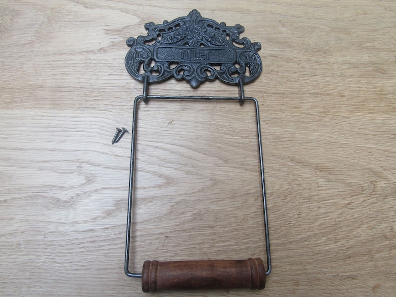 May include: Black cast iron toilet paper holder with a decorative scroll design and the word "Toilet" on the top. The holder has a wooden dowel for hanging the paper roll.