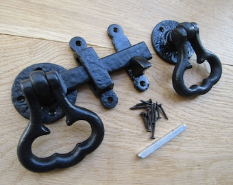 May include: Black metal gate latch with a decorative handle. The latch has a square shape and a lever that can be moved to lock or unlock the gate. The handle is shaped like a heart and has a loop for easy gripping. The latch is designed for use on gates, fences, and other outdoor structures.