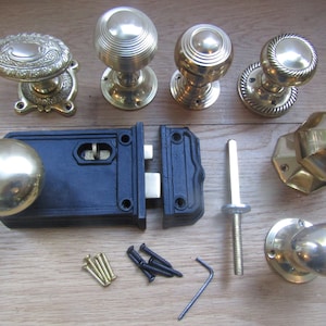 Puede incluir: Un juego de pomos de puerta de latón y un pestillo de puerta negro con tornillos y una llave Allen. Los pomos de puerta tienen diferentes diseños, incluyendo un pomo redondo, un pomo con un patrón decorativo y un pomo con un diseño geométrico.