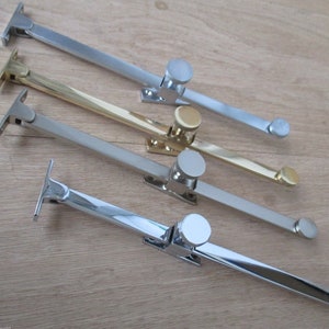 Pode incluir: Quatro fechos de janela em diferentes acabamentos: prata, ouro, níquel polido e cromo. Cada fecho tem um botão redondo e um braço plano.