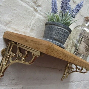 May include: A wooden shelf with ornate gold metal brackets. The shelf is decorated with a small potted plant and a clear glass bottle with a butterfly design.