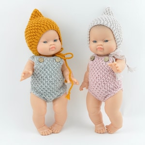 Puede incluir: Dos conjuntos de muñeca de punto con gorros a juego. Un conjunto es gris con un gorro amarillo y el otro es rosa con un gorro gris.