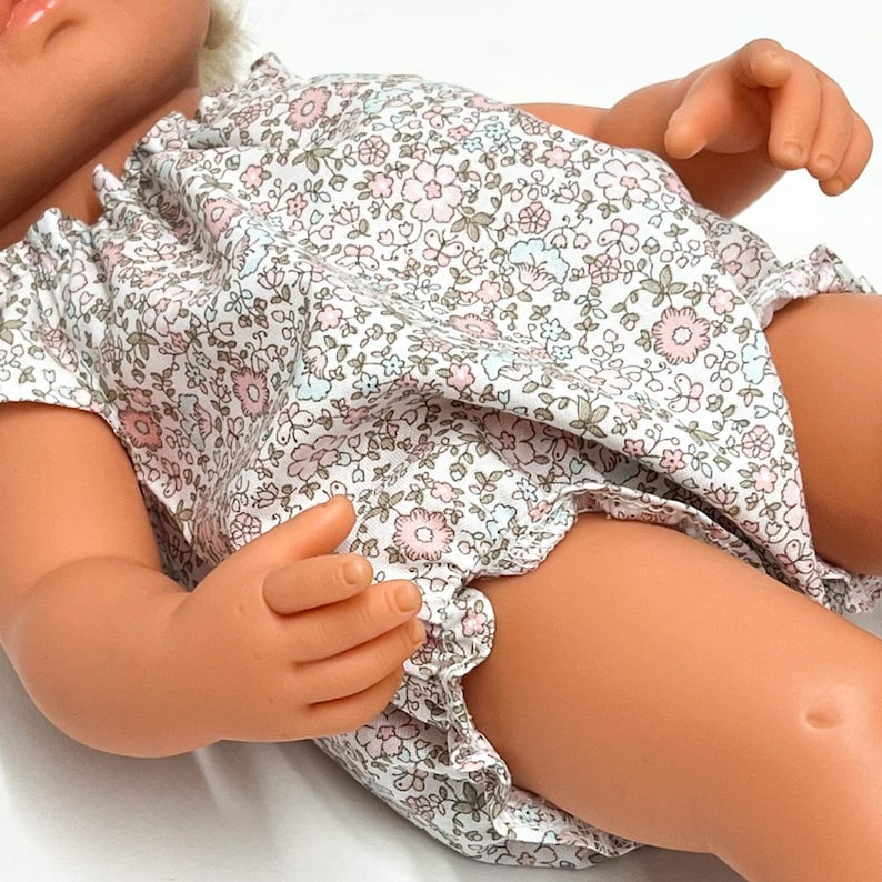 May include: A white baby doll romper with a floral print in shades of pink, blue, and brown. The romper has a ruffled neckline and a gathered skirt.
