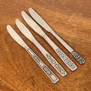 May include: Four silver dinner knives with ornate black designs on the handles.