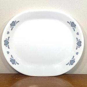 May include: An oval white serving platter featuring a repeating pattern of blue hearts along the rim. The hearts are stylized with a dotted texture and small curved accents, creating a symmetrical border around the smooth, plain center of the dish.