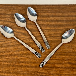 May include: Four silver teaspoons with ornate floral designs on the handles. The spoons are arranged in a fan shape on a wooden surface.