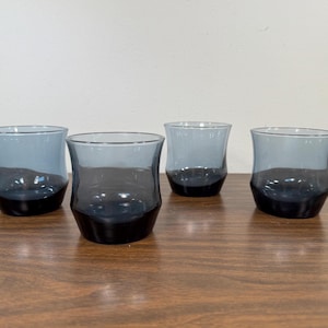 May include: Four clear glass tumblers with a dark blue tint. The glasses are on a wooden surface.
