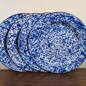 May include: Four blue and white speckled enamelware plates with black rims are stacked on a wooden surface. The plates have a classic speckled design, with a dark blue pattern on a white background. The plates are a classic kitchenware item.