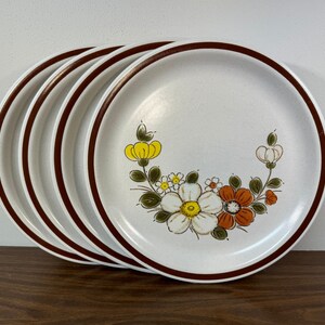 May include: Set of four white ceramic dinner plates with a brown rim and a floral design featuring yellow, white, and orange flowers.