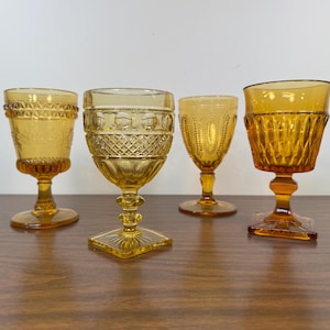May include: Four amber glass goblets with different patterns. The goblets have a round bowl and a stem with a flared base.