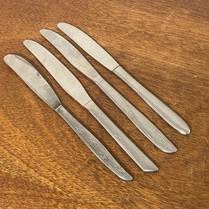 May include: Four silver butter knives with a starburst pattern on the blade.