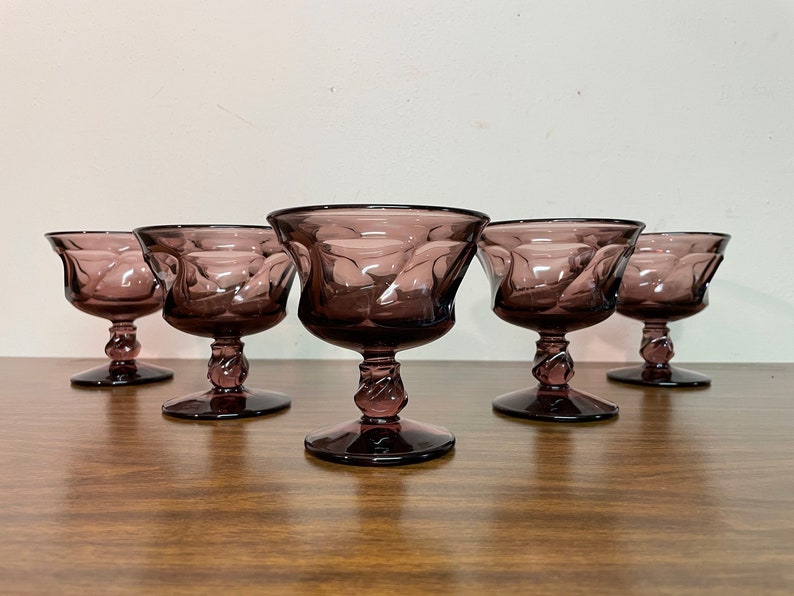 May include: Set of six purple glass dessert cups with a swirl design. The cups have a stemmed base and are perfect for serving ice cream, pudding, or other desserts.