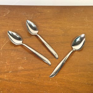 May include: Three silver-toned stainless steel grapefruit spoons with serrated edges at the tips. Each spoon features a polished finish and a small, engraved starburst pattern on the handle, designed for segmenting citrus fruit.