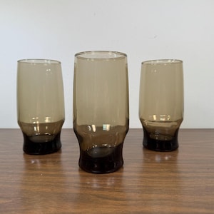 May include: Three brown glass tumblers with a rounded bottom and a flared top.