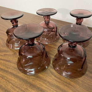 May include: Five clear, amethyst-colored glass dessert dishes with a swirl design. The dishes have a footed base.