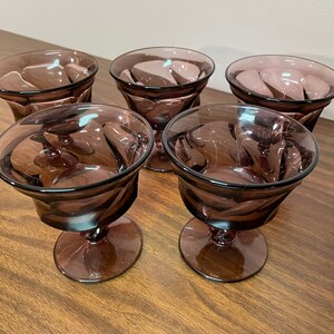 May include: Set of five purple glass dessert cups with a swirl design. The cups have a stemmed base.