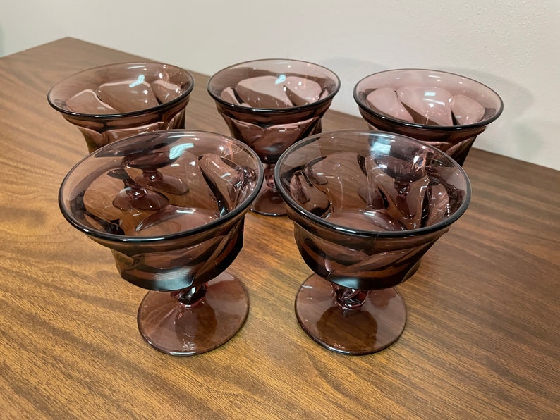 May include: Set of five purple glass dessert cups with a swirl design. The cups have a stemmed base.