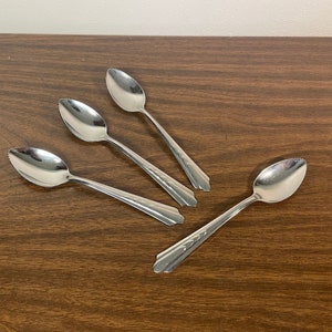 May include: Four silver citrus spoons with serrated edges on a brown wooden surface.