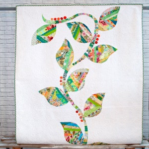 May include: A white quilt with a green and orange vine design. The vine is made of fabric scraps and has leaves that are different shapes and sizes. The leaves are a mix of green, blue, and yellow fabrics.